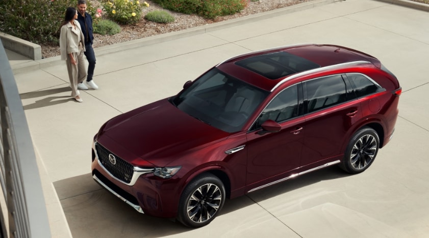 Couple walking toward a parked red Mazda CX-90 SUV in a driveway.