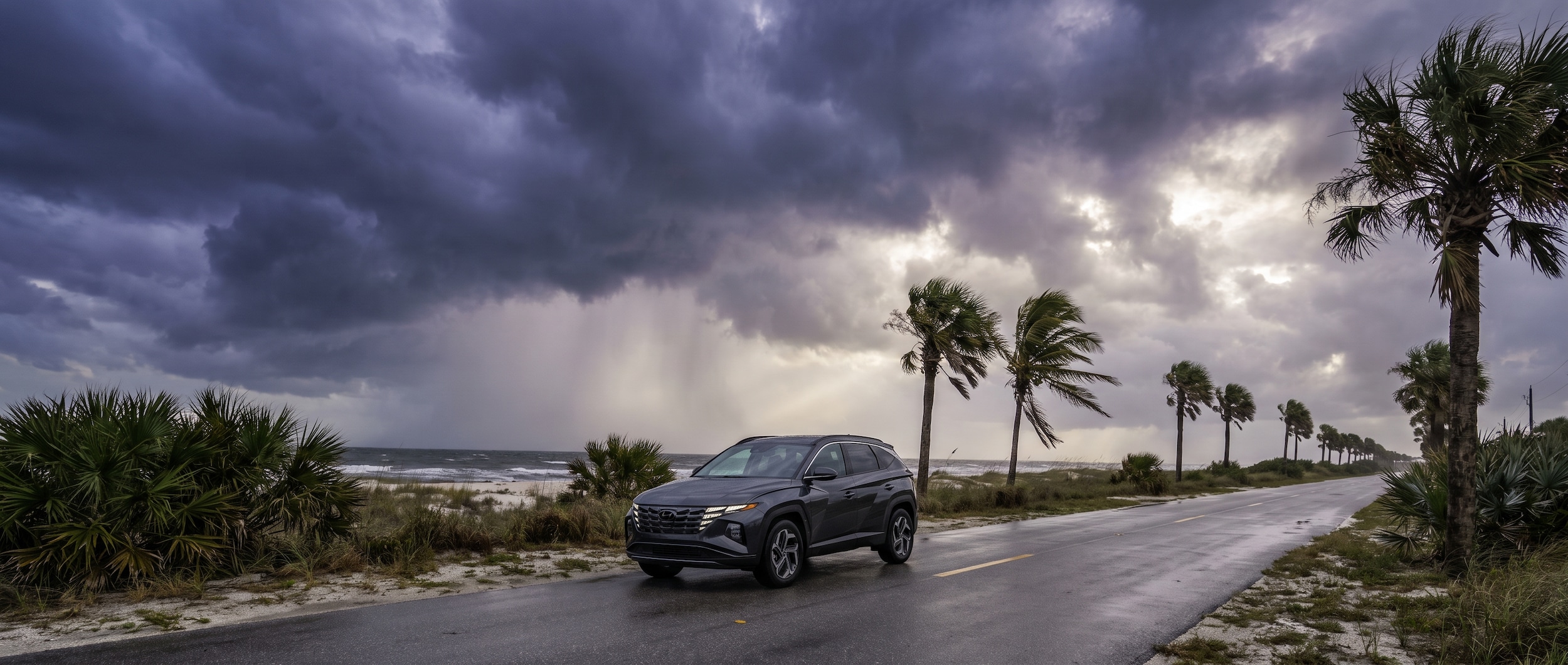 A 2026 Hyundai Tucson in dark gray parked on a Florida Gulf Coast road under heavy storm clouds, dramatic pre-hurricane sky, palm trees bending in wind, coastal road setting