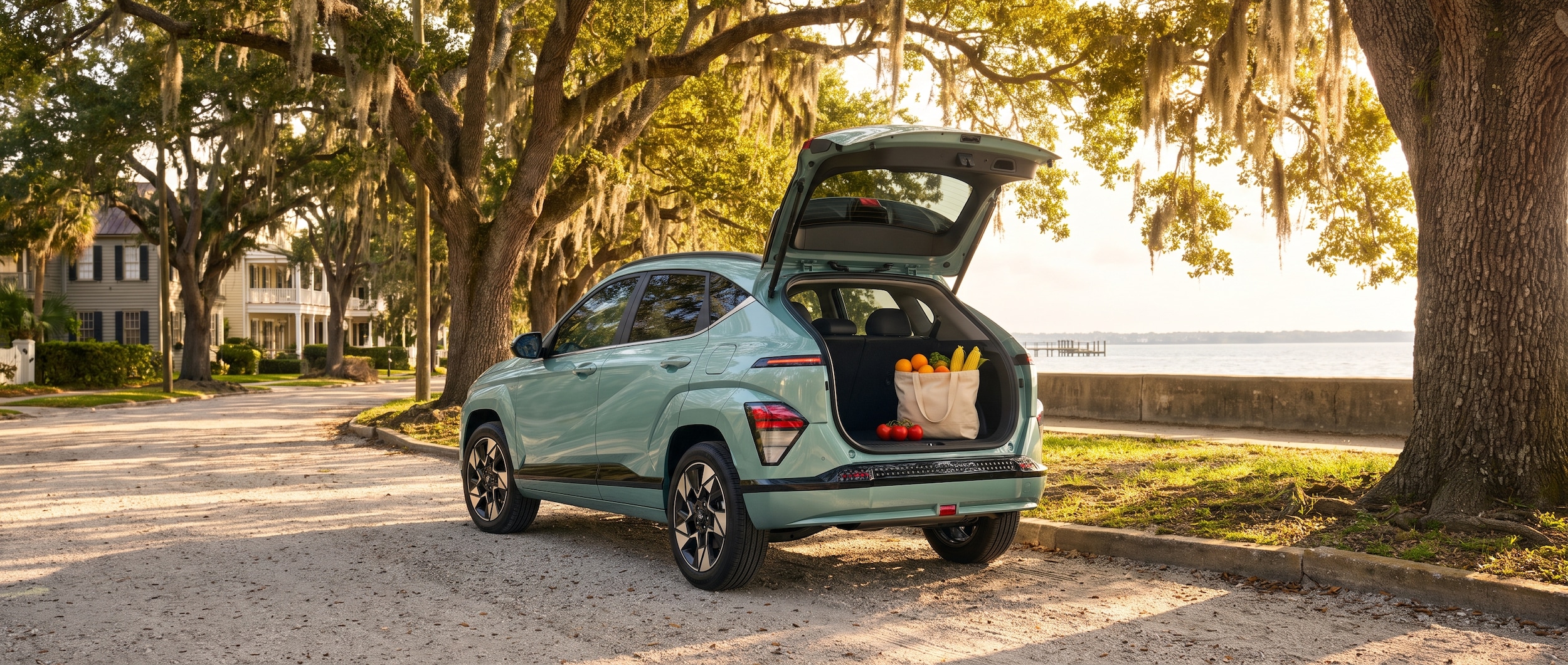 A 2026 Hyundai Kona parked along a shaded waterfront street in a historic Florida coastal neighborhood on a bright summer morning, tailgate area visible with a canvas tote and fresh produce, lush green oaks in the background, warm golden light