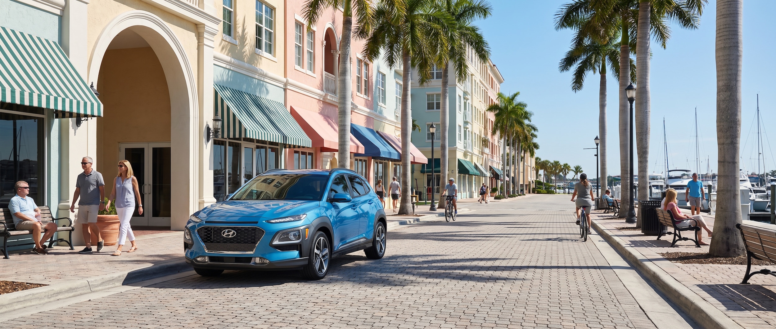A compact Hyundai Kona parked near a charming waterfront street lined with historic storefronts, palm trees, and pedestrians enjoying a sunny Florida day.