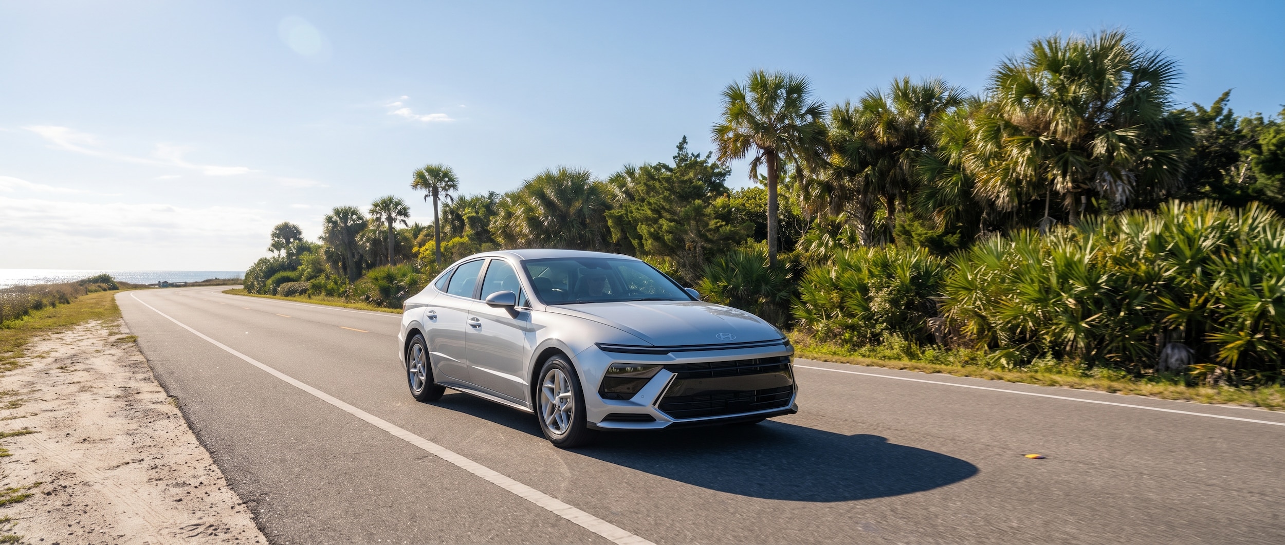 A 2026 Hyundai Sonata in a silver or white finish driving on a sun-drenched Florida coastal highway with bright blue sky and lush green vegetation on the shoulder, evoking a Gulf Coast summer morning commute