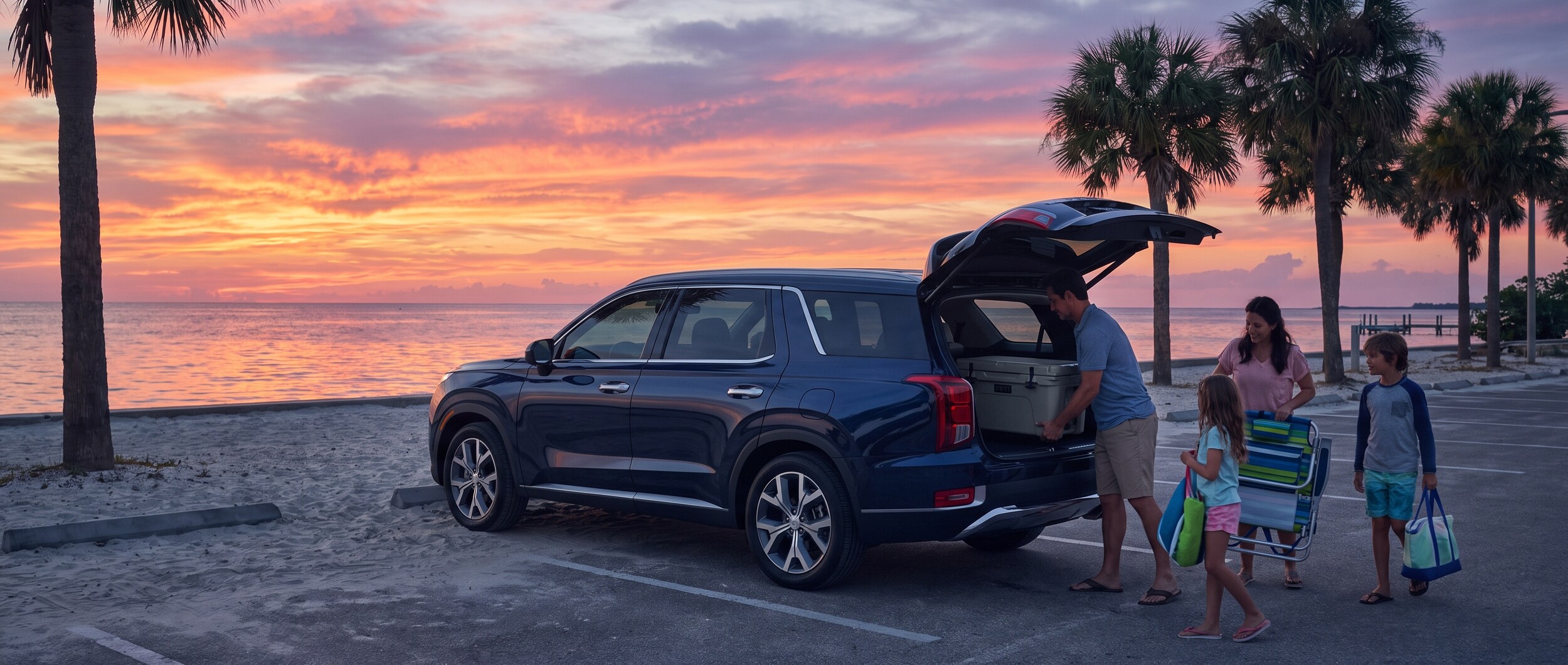 A family loading beach chairs and a cooler into a large Hyundai SUV in a waterfront parking area at dusk, with a colorful sunset reflecting off the water in the background, palm trees lining the lot.
