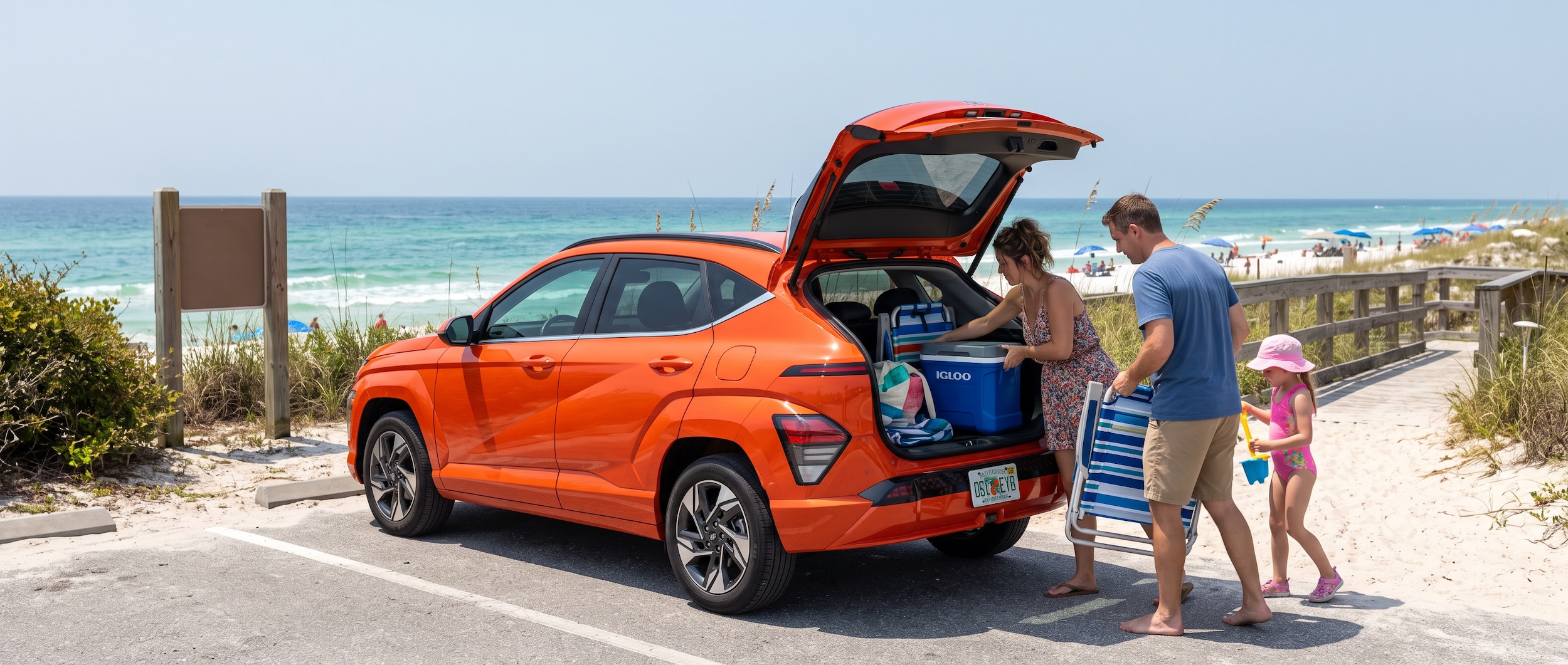 A 2026 Hyundai Kona in a bold exterior color parked near a Florida Gulf Coast beach access point on a bright, hazy August morning, with a family loading beach chairs and a cooler into the open rear liftgate, blue-green Gulf water visible in the background and a clear summer sky overhead.