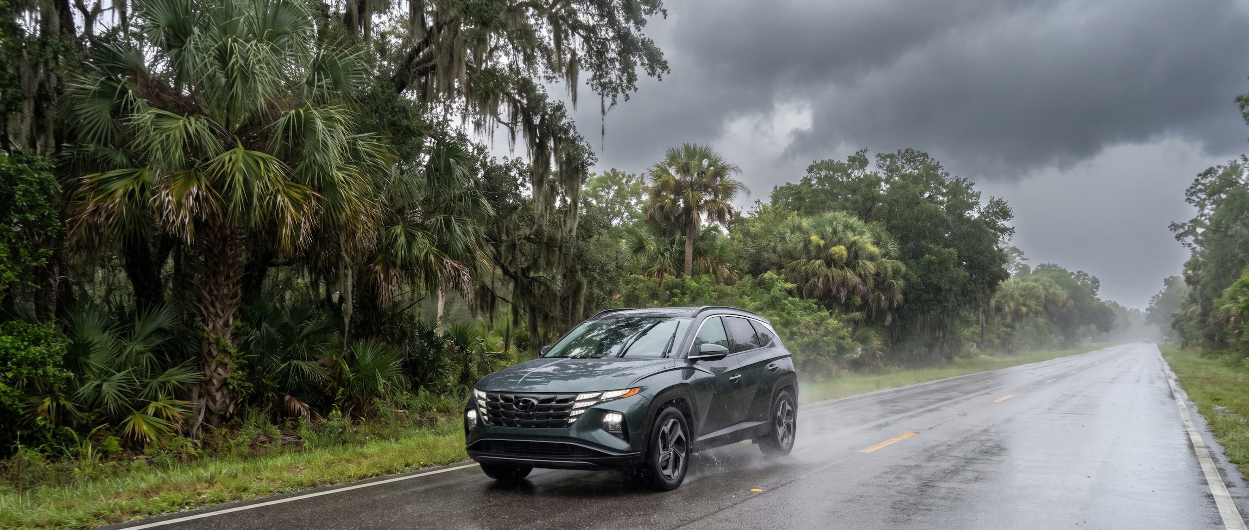 A 2026 Hyundai Tucson driving on a wet Florida road during a summer thunderstorm, water spraying from the tires, overcast sky, lush Gulf Coast greenery along the roadside