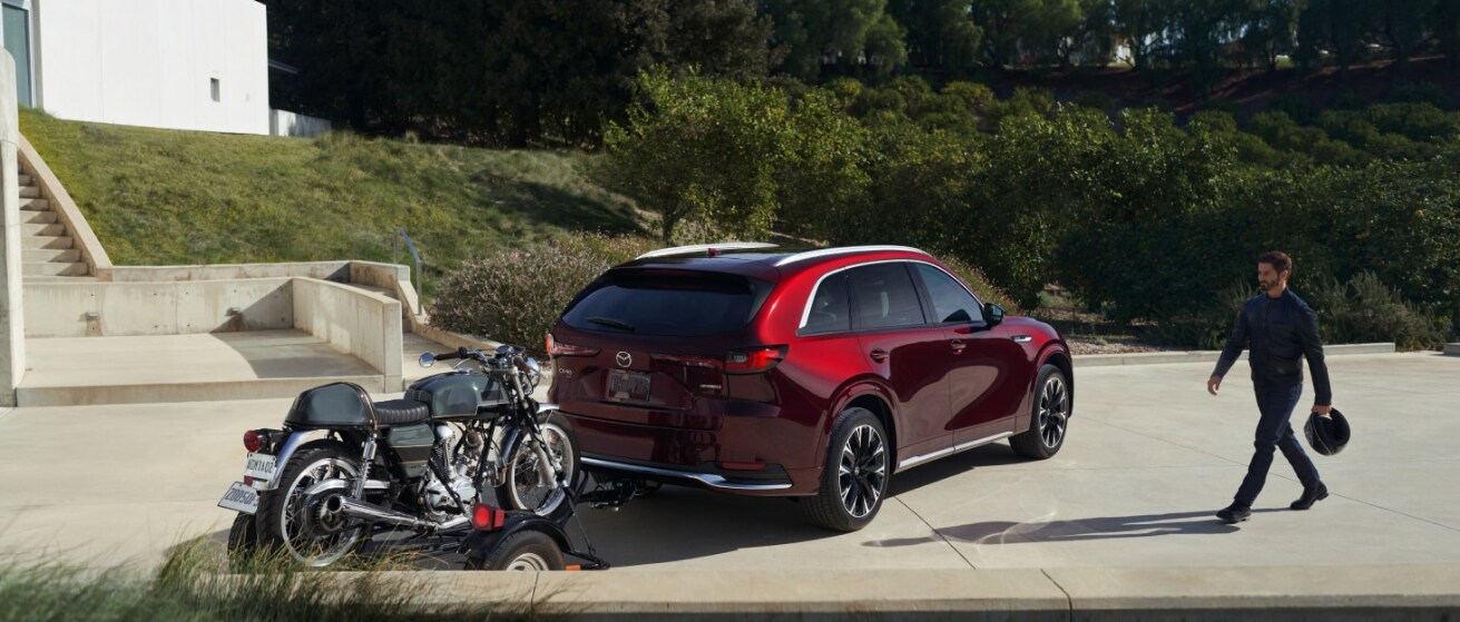 Screenshot 2025-08-21 142836.png 2025 red Mazda CX-90 with motoecycle attacted in the back parked.