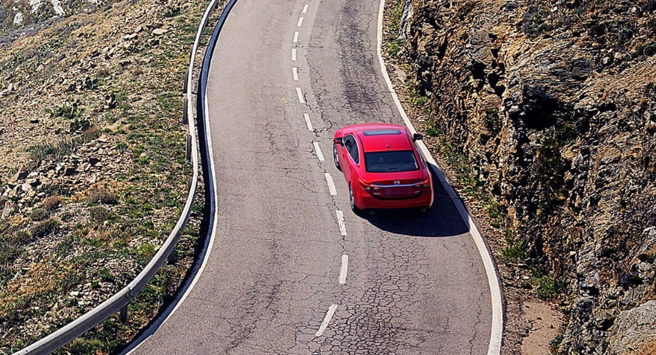 Red Mazda driving down curvy highway, ariel view.