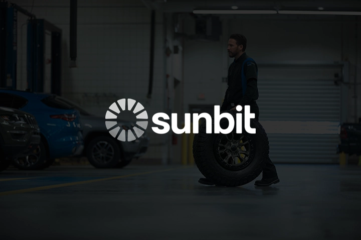 Sunbit logo overlayed on top of an image of a Mopar service technician rolling a tire and wheel across the shop floor