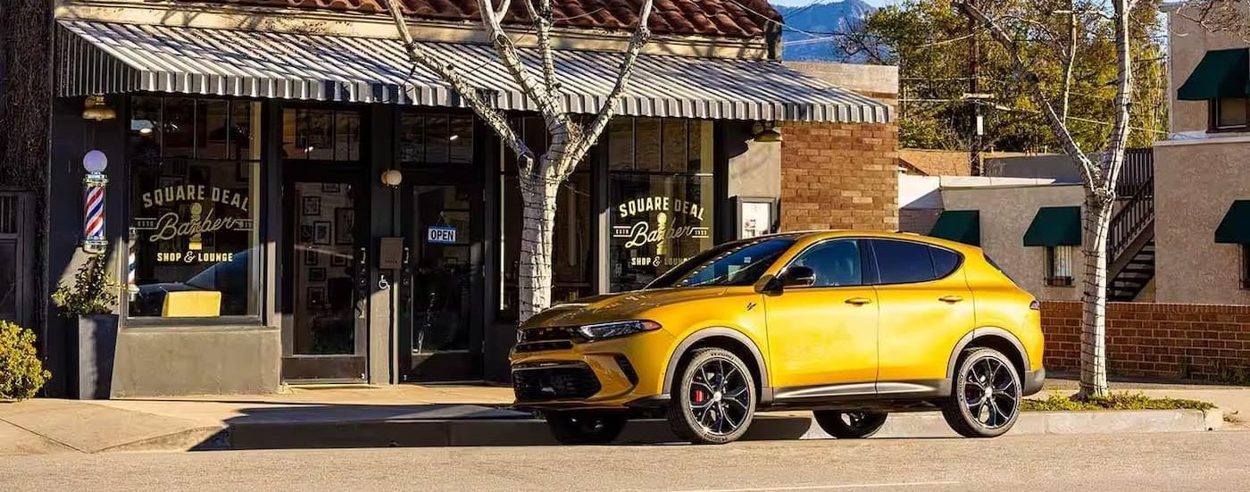 A yellow 2024 Dodge Hornet parked by a city curb.