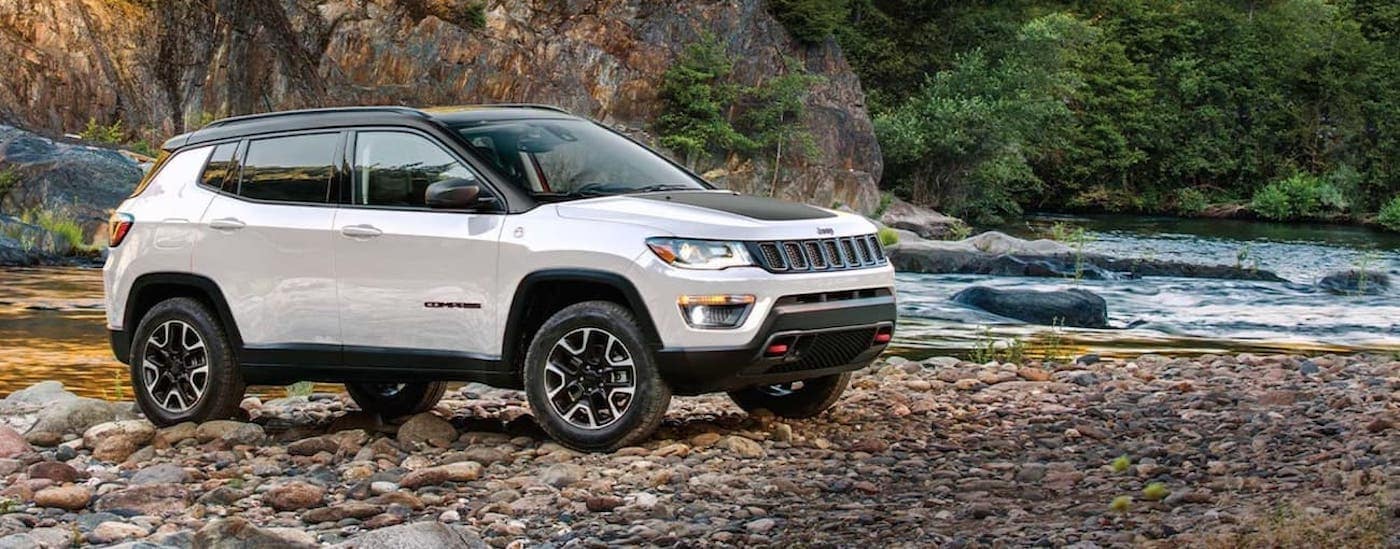 A white 2020 Jeep Compass Trailhawk parked off-road by a river.