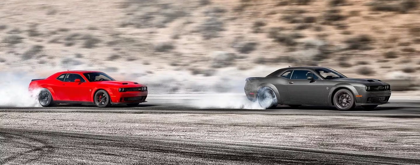 A red and a grey 2024 Dodge Challenger Hellcat Widebody are shown performing burnouts after leaving a Dodge dealership.