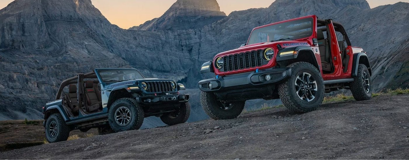 A grey and a red 2025 Jeep Wrangler for sale parked off-road.