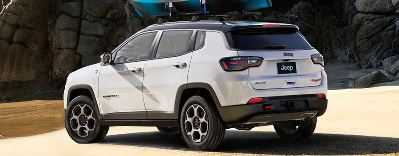 Rear view of a white 2022 Jeep Compass parked off-road by a lake.