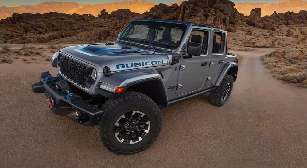 A silver 2024 Jeep Wrangler 4xe Rubicon is shown parked off-road after visiting a Jeep dealer.