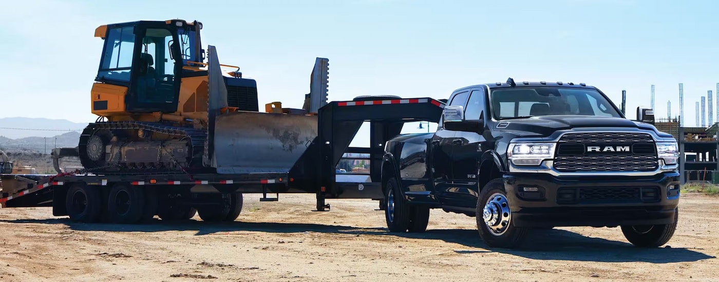 A black 2024 Ram 3500 towing a bulldozer on a gooseneck trailer.