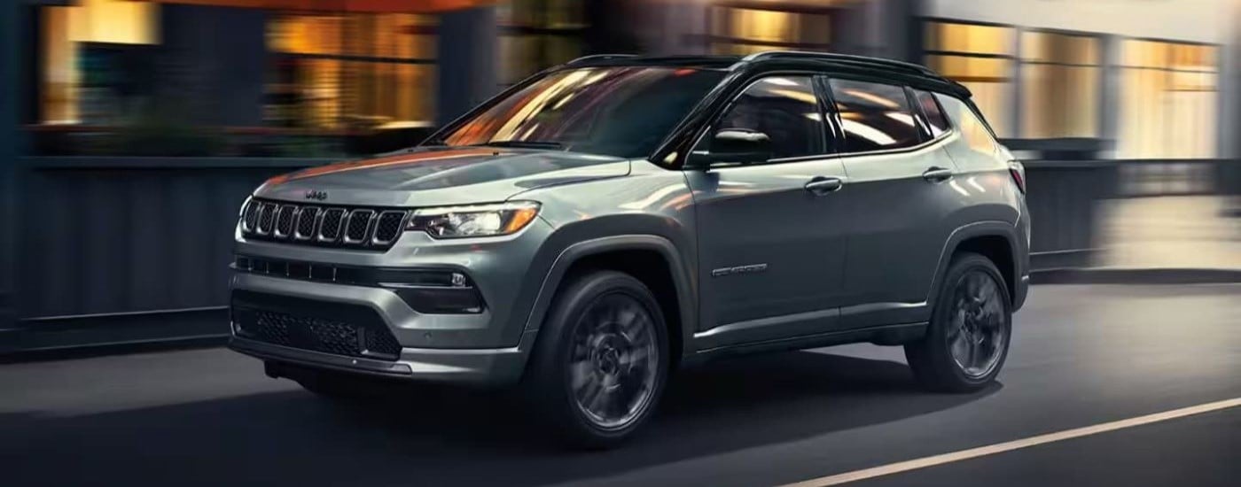 A grey 2023 Jeep Compass for sale driving down a road.