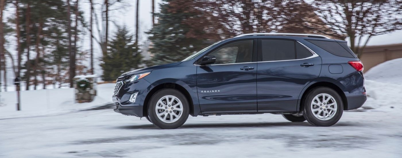 A blue 2018 Chevy Equinox is shown from the side driving on a snowy road.