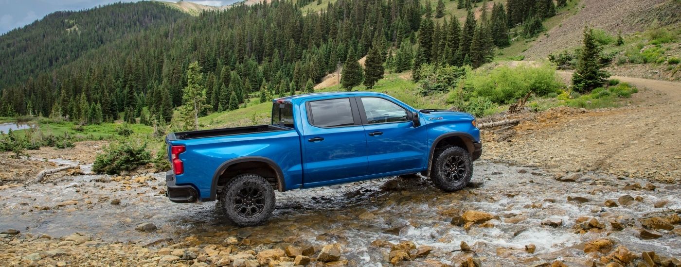 A blue 2024 Chevy Silverado 1500 ZR2 crossing a shallow stream while off-roading.