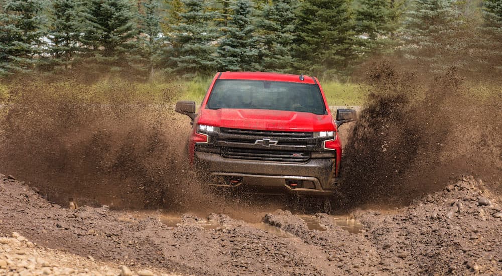 A red 2024 Chevy Silverado 1500 LT Trail Boss driving through a puddle of mud.