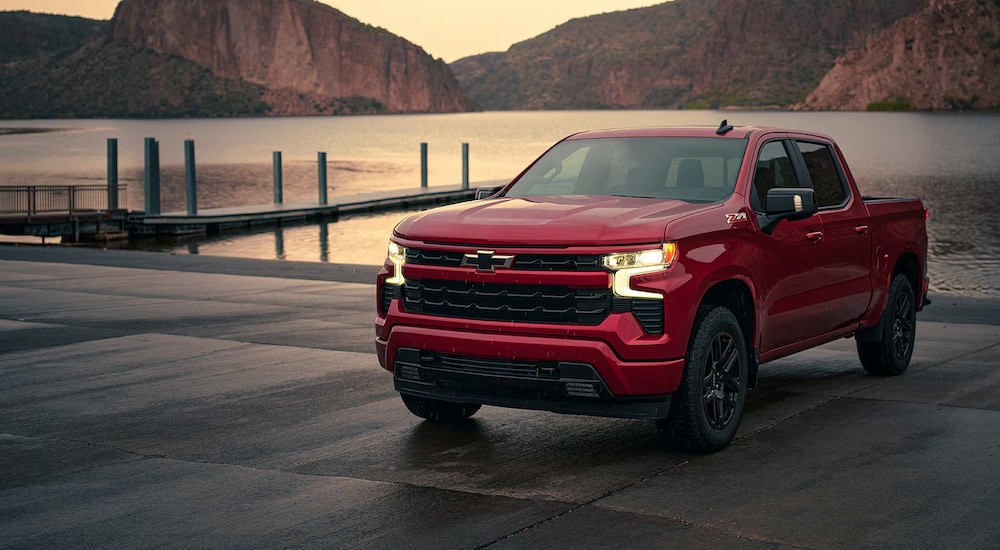 A red 2024 Chevy Silverado 1500 RST parked near a lakeside boat launch.