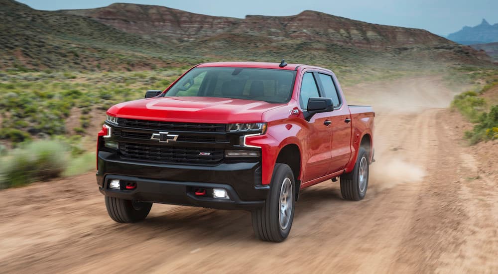 A red 2024 Chevy Silverado 1500 LT Trail Boss driving on a dirt road.
