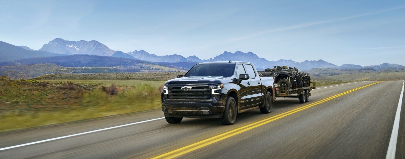 A black 2025 Chevy Silverado 1500 for sale near Northampton is shown from the front at an angle, while towing ATVs.