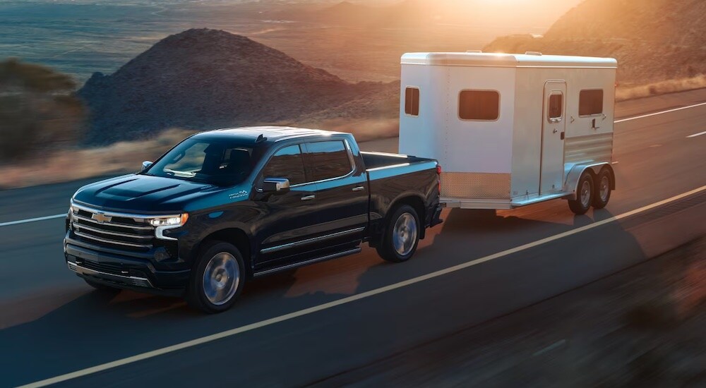 A black 2024 Chevy Silverado 1500 High Country towing a trailer.