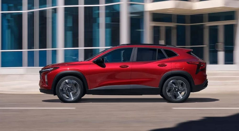 A red 2024 Chevy Trax is shown driving near a building.
