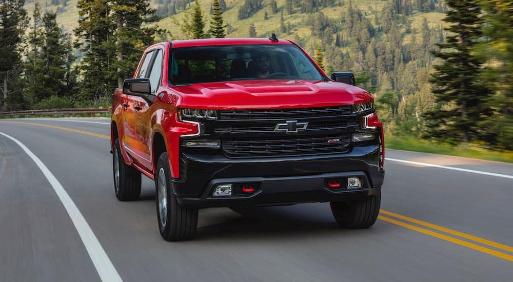 A red 2024 Chevy Silverado 1500 LT Trail Boss driving around a bend.