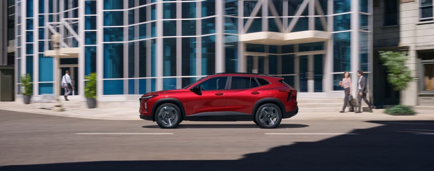 A red 2025 Chevy Trax 2RS is shown driving in a city.