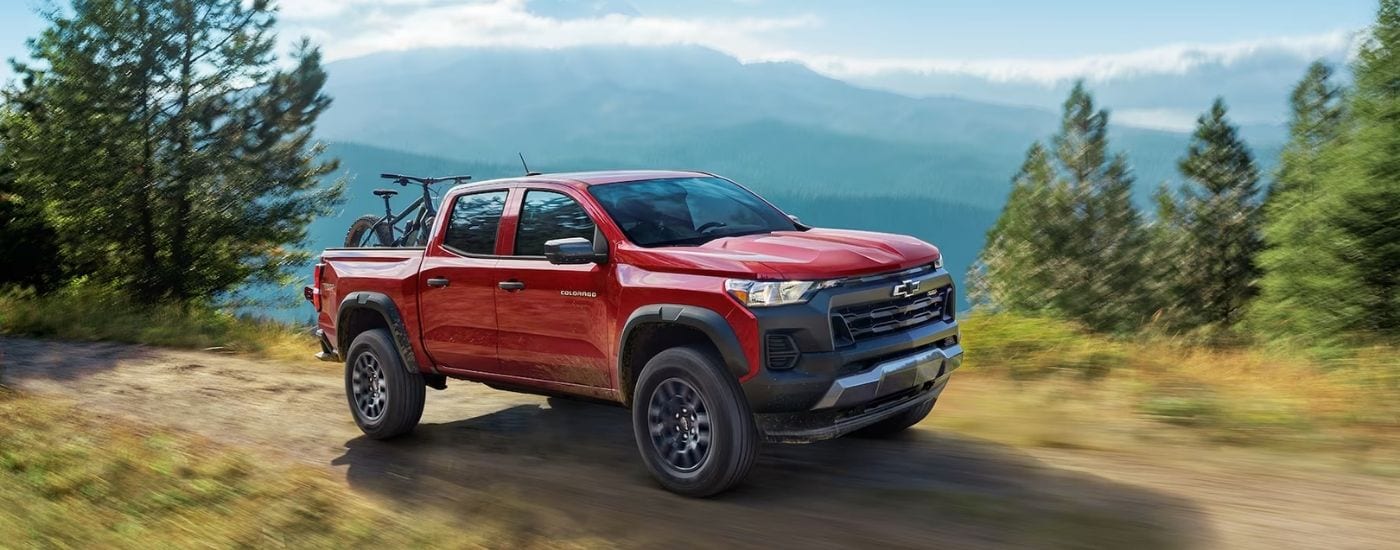 A red 2024 Chevy Colorado Trail Boss driving on a mountain trail with bikes in the bed.