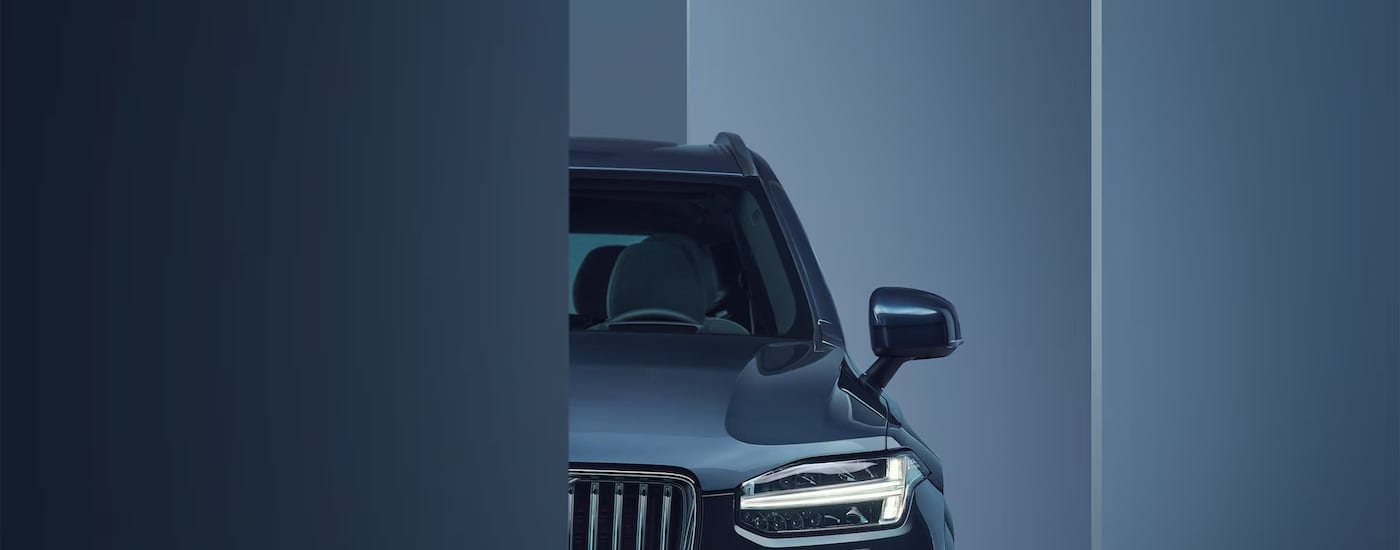 A close up of the front side of a 2024 Volvo XC90 is shown halfway behind a wall.