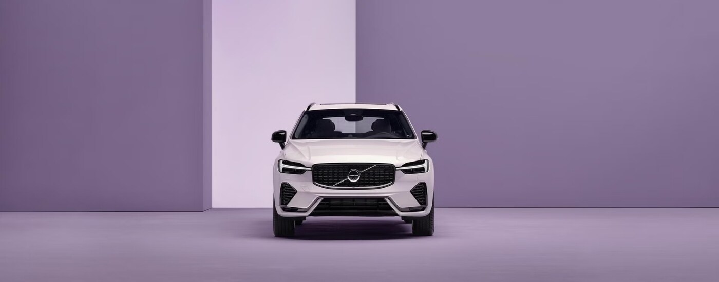 Head-on view of a white 2025 Volvo XC60 PHEV in front of a purple background.