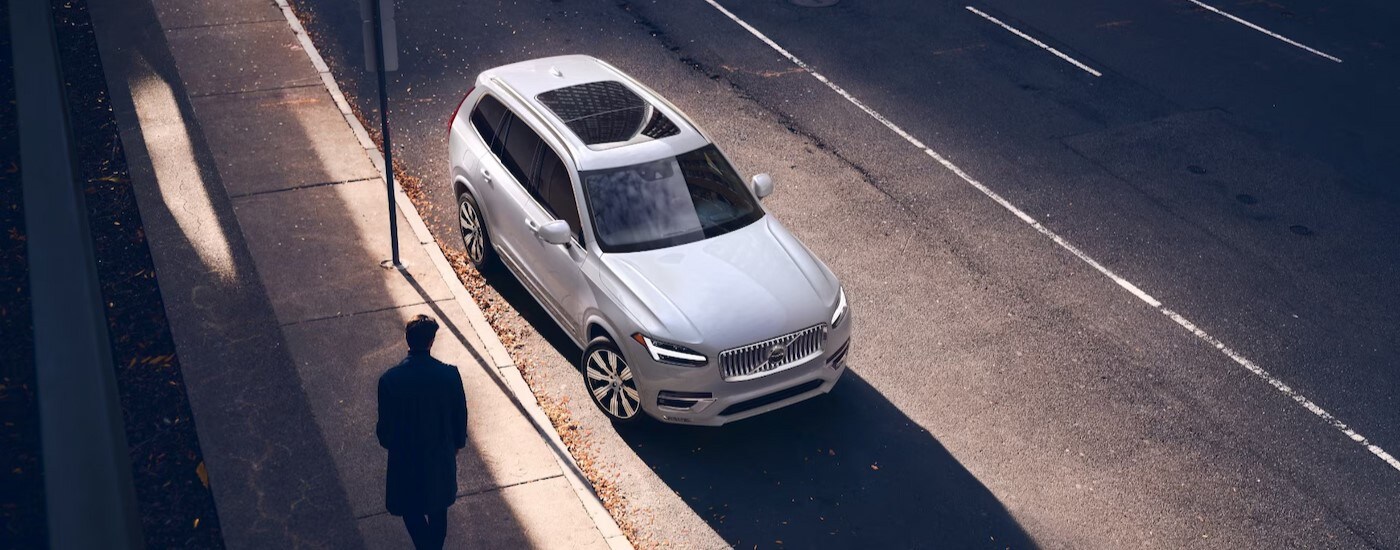 A white 2025 Volvo XC90 is shown parked near a person walking.