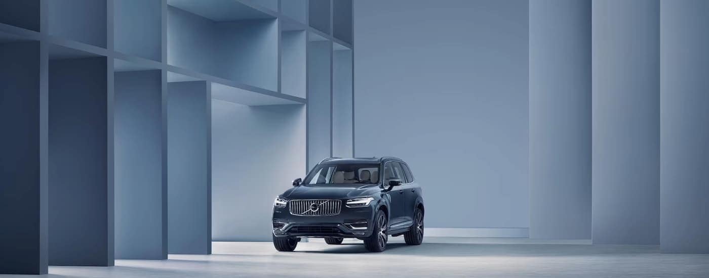 A blue 2024 Volvo XC90 parked among dramatic architecture.
