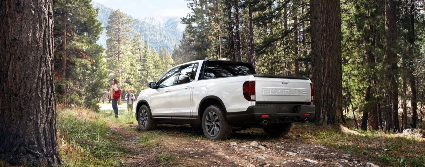 A white 2024 Honda Ridgeline is shown on a trail in the woods after leaving a Honda dealership.