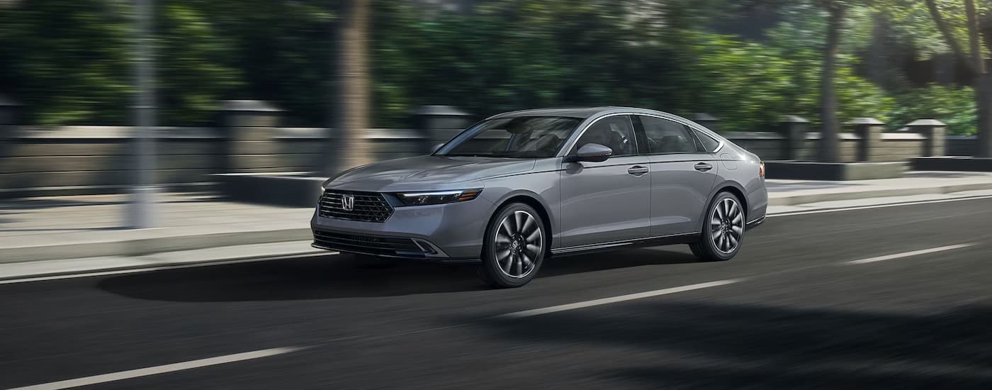 A grey 2023 Honda Accord Touring Hybrid is shown driving on a city street.