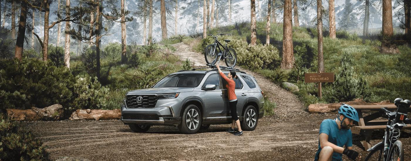 A grey 2023 Honda Pilot Trailsport is parked in a hiking trail parking lot.