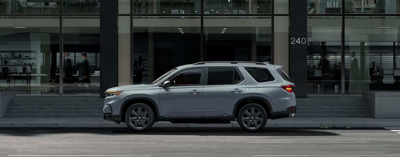 A grey 2025 Honda Pilot is parked on the side of a city street.
