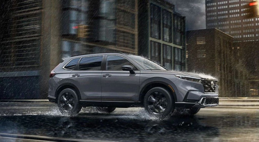 A grey 2024 Honda CR-V Sport Touring Hybrid driving in a rainy city.