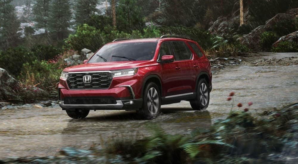A red 2025 Honda Pilot is shown driving on a rainy day.