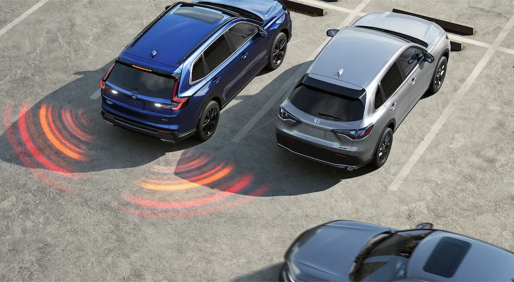 A blue 2025 Honda CR-V Sport Touring Hybrid is reversing in a busy parking lot.