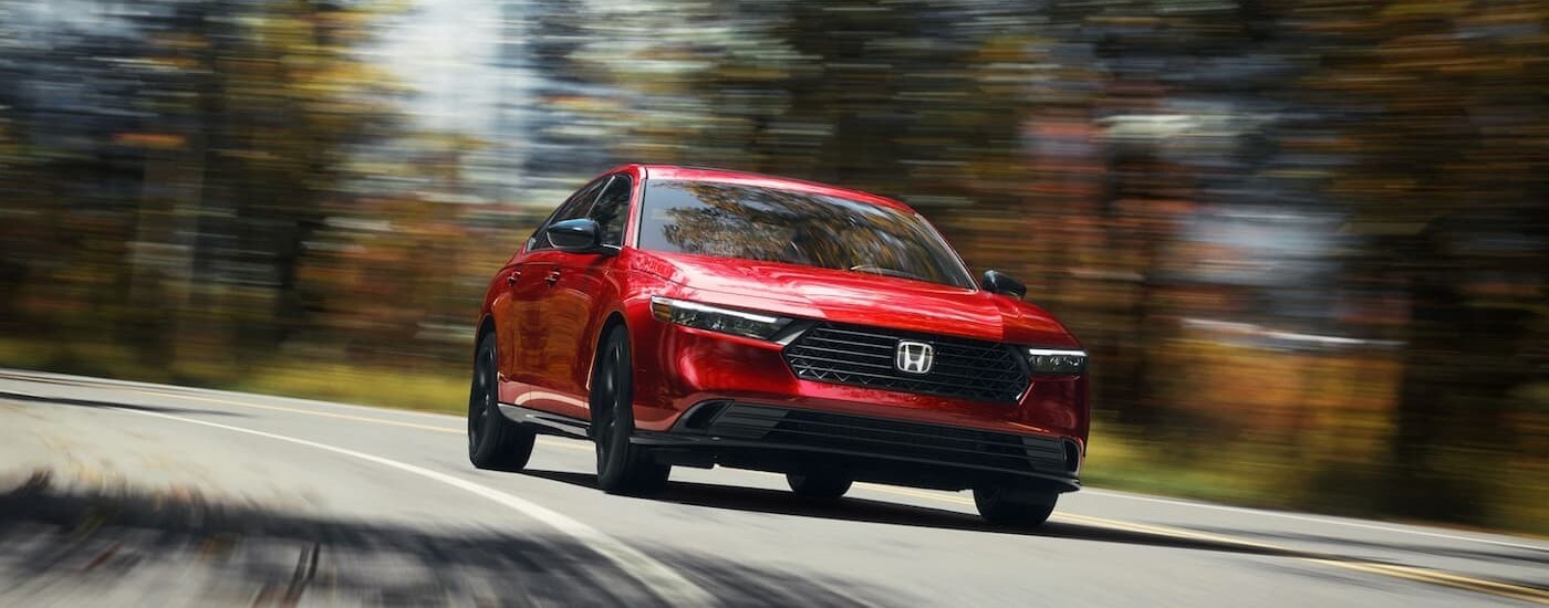 A red 2025 Honda Accord Sport-L Hybrid is shown driving on a highway.