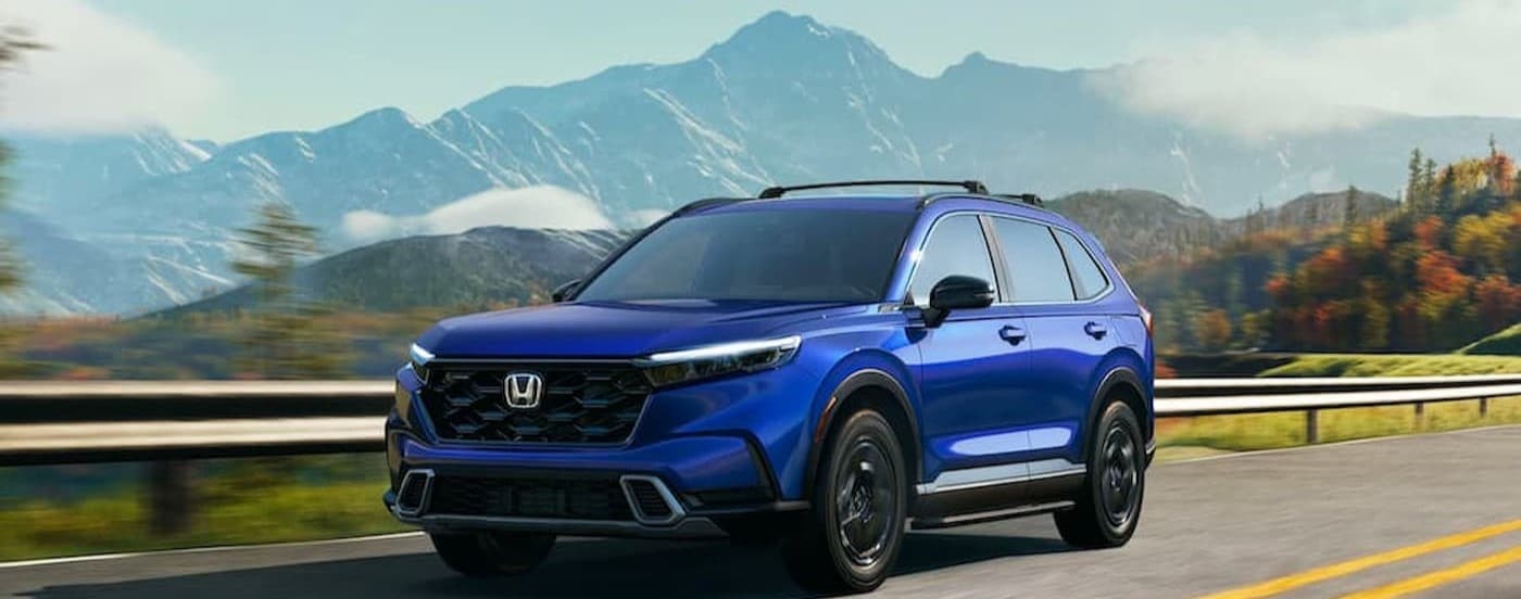 A blue 2023 Honda CR-V Sport Touring is shown driving on a highway.