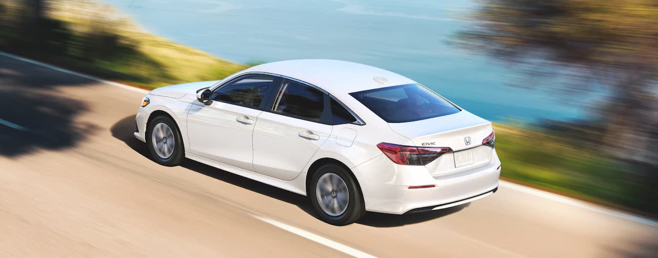 High rear angle view of a white 2022 Honda Civic LX driving down a road.