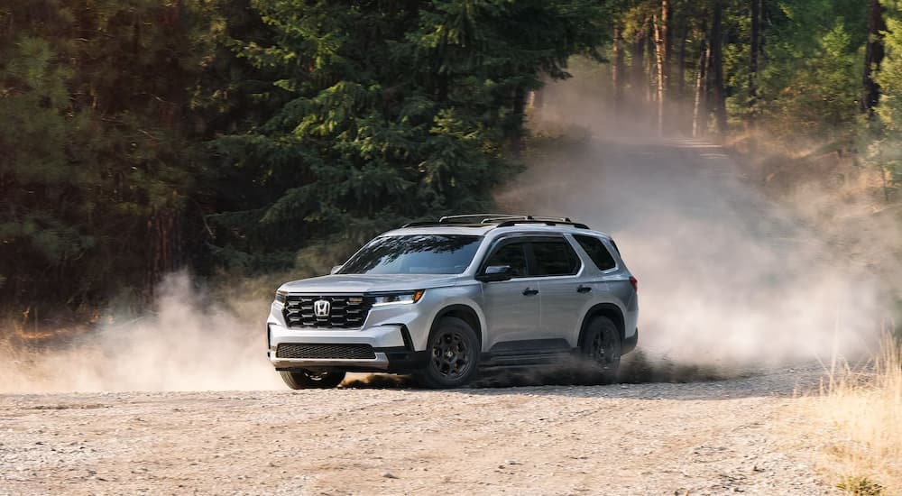A grey 2025 Honda Pilot Trailsport for sale driving on a dusty path.