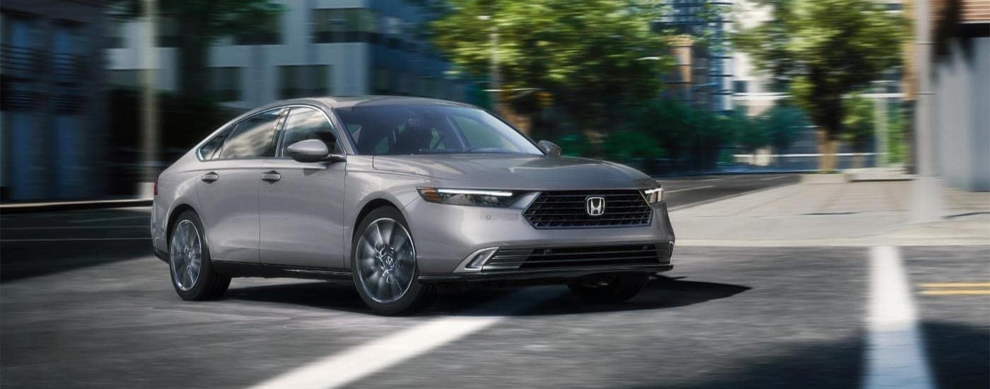 A grey 2024 Honda Accord Touring Hybrid driving in a city intersection after visiting a Honda dealer near Bennington.