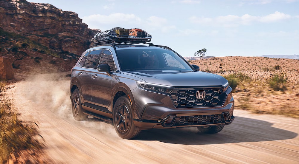 A silver 2025 Honda CR-V Sport Hybrid driving on a dusty dirt road.