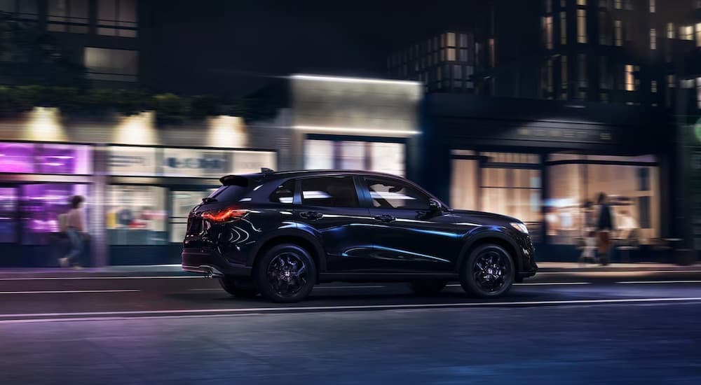 A black 2024 Honda HR-V for sale is shown from the side on a city street.