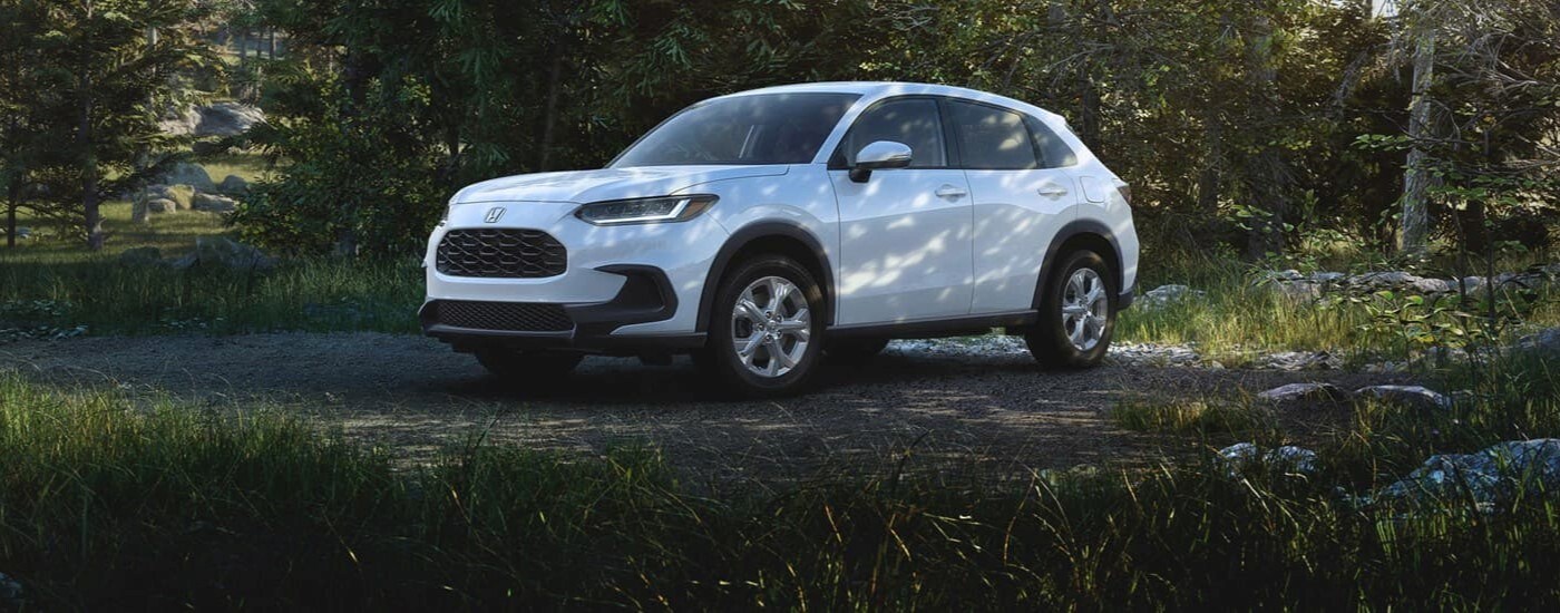 A white 2024 Honda HR-V for sale is shown parked near the forest.