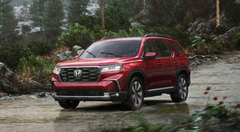 A red 2025 Honda Pilot Elite driving on a dirt road during a rainstorm.